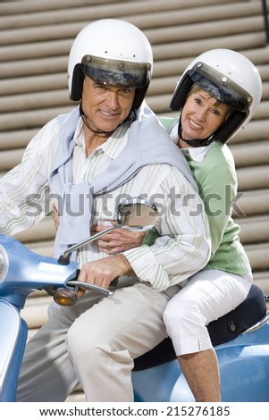 Senior couple riding on blue motor scooter near urban steps, smiling, side view, portrait (tilt)