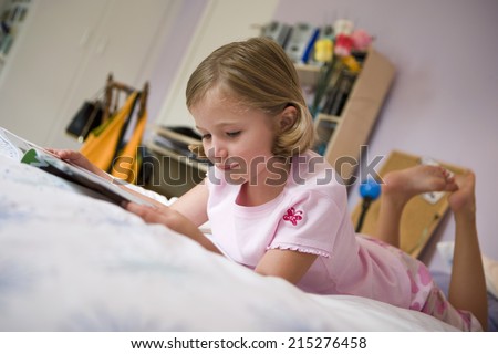 Girl (6-8) lying on bed, reading book, side view, surface level (tilt)