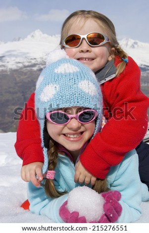 Two girls (6-8) together in snow field, wearing sunglasses, smiling, portrait, mountain range in background