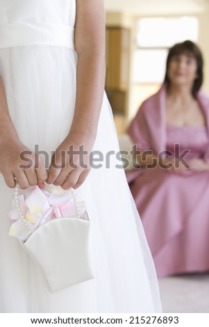 Senior woman, in pink dress, looking at bridesmaid (8-10) holding wedding gift, focus on foreground