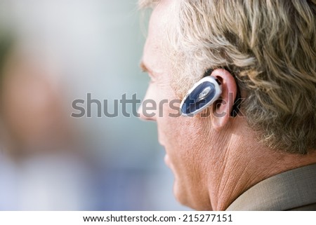 Mature businessman wearing mobile phone hands-free device, close-up, profile