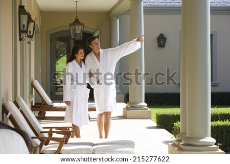 Couple wearing white robes, standing on verandah, man pointing