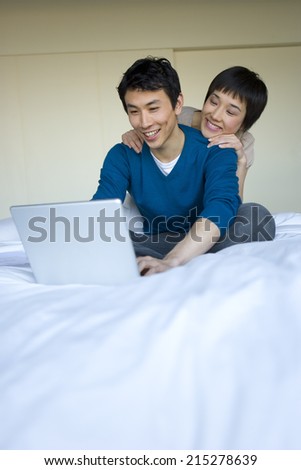 Young woman embracing young man using laptop on bed, smiling
