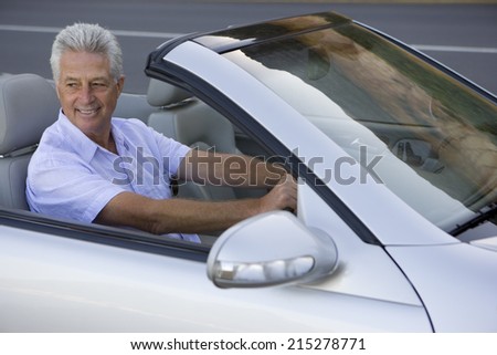 Senior man driving silver convertible car, smiling, side view