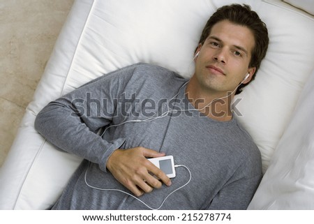 Man relaxing on sofa at home, listening to MP3 player, smiling, portrait, overhead view