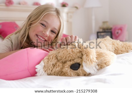Girl (6-8) on bed with toy dog, smiling, portrait