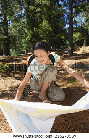 Woman crouching on lakeside woodland trail, looking at map, smiling