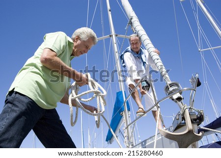 Two mature men preparing to set sail on yacht, one man untying mooring rope, smiling, low angle view