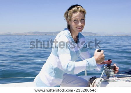Woman winding rope pulley of boat rigging on deck of sailing boat out at sea, smiling, side view, portrait