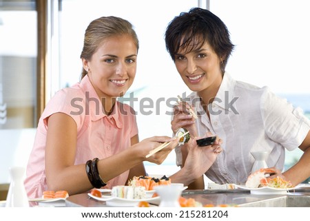Two women eating in sushi bar, smiling, portrait