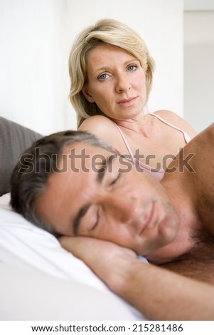 Couple on bed, man asleep in foreground, portrait of woman in background