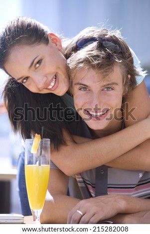 Young woman embracing young man sitting with drink in cafe, smiling, portrait