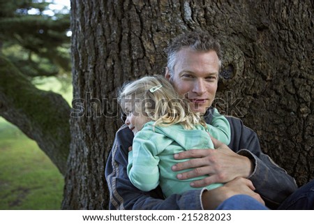 Father embracing daughter (3-5) beside tree in garden, smiling