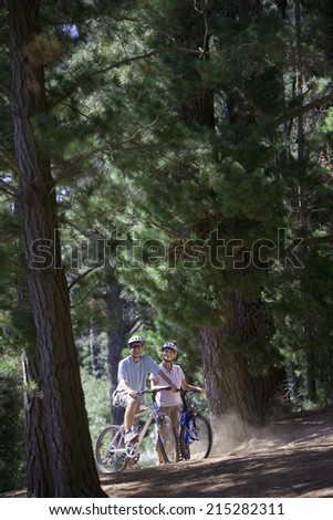 Mature couple, in mid-distance, mountain biking along woodland trail, smiling, side view, portrait