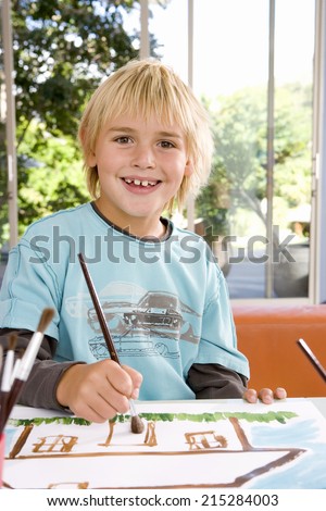 Boy (6-8) painting picture of house, smiling, portrait
