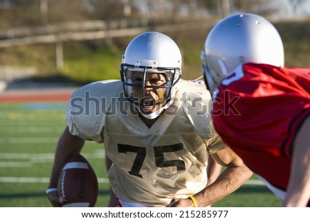 Determined American football player running with ball at opposing players during competitive game, snarling ferociously, front view