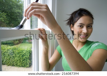 Young woman painting window frame, smiling, portrait, close-up