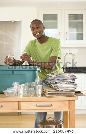 Young man putting empty glass jar and can into recycling bin in kitchen, smiling, portrait