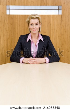Businesswoman at conference table, hands clasped, portrait