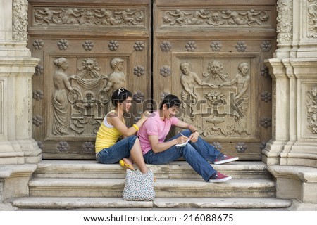 Couple on steps by wooden doors writing, smiling, side view