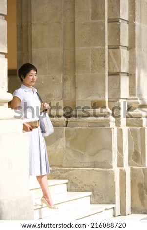 Young woman on steps with bag and newspaper, side view