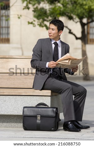 Businessman with briefcase and newspaper on park bench, looking over shoulder