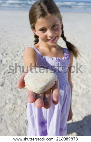 Girl (5-7) with shell on beach, smiling, portrait (differential focus)