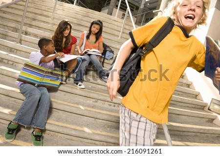 Small group of teenagers (13-15) studying on steps outdoors by boy (11-13) with rucksack
