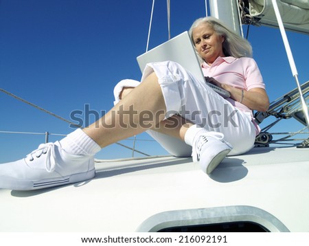 Mature woman using laptop computer on boat, low angle view