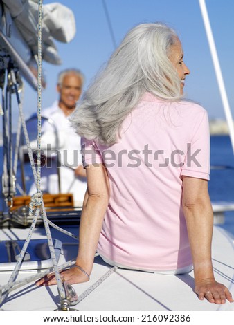 Mature woman reclining on deck of boat by man at wheel, rear view