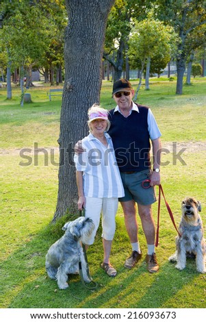 Senior couple arm in arm with dogs in park, smiling, portrait