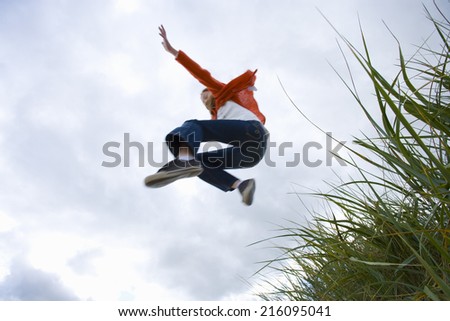 Girl (7-9 years) jumping from grass outdoors, low angle view