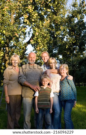 Family of three generations arm in arm in orchard, smiling, portrait