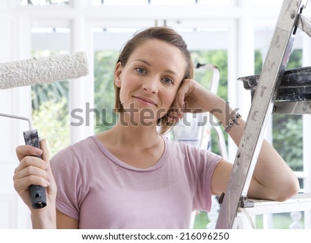 Woman by ladder with paint roller, smiling, portrait