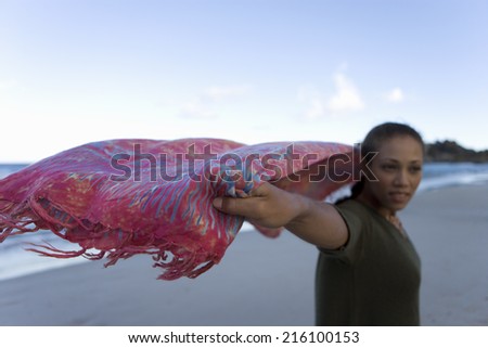 Woman with sarong flying in wind on beach, smiling (differential focus)