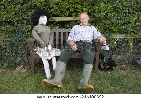 Senior man with eyes closed by scarecrow on bench