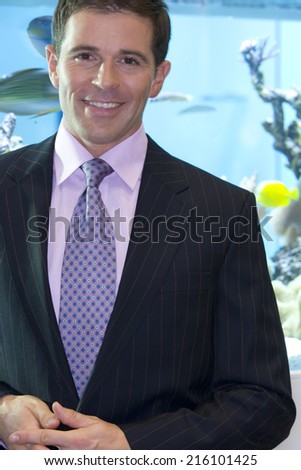 Businessman by fish tank, smiling, portrait