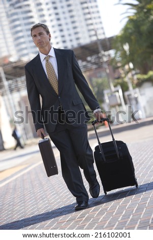 Businessman wheeling luggage in urban setting