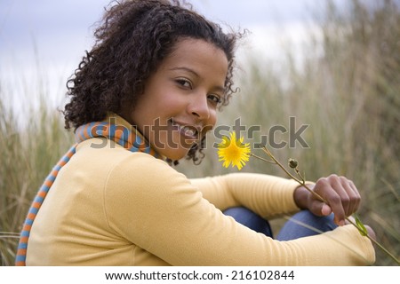 Woman with flower on sand dune, smiling, portrait
