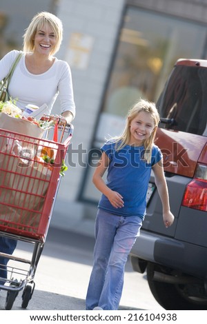 Mother with daughter pushing grocery cart full of groceries