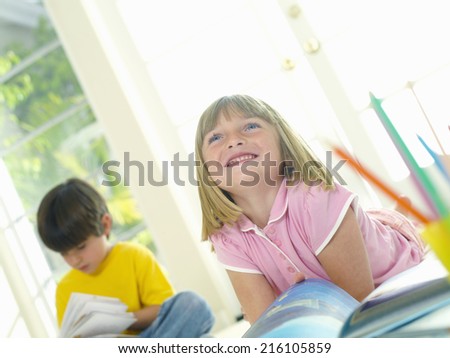 Girl (4-6) with book by friend (4-6), smiling, low angle view (tilt)