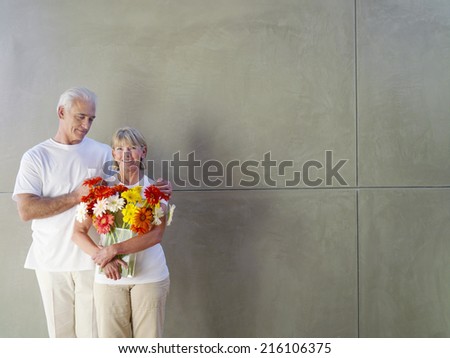 Mature man with hands on woman\'s shoulders, woman with vase of flowers, smiling, portrait