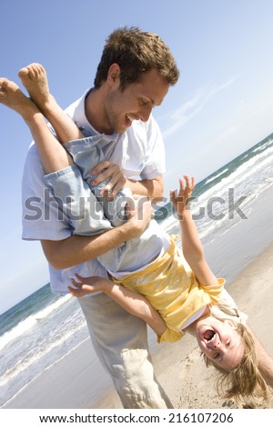 Father holding daughter upside down on beach