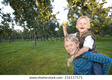 Girl (11-13) giving brother piggy back, boy with apple, smiling, portrait