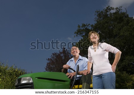 Senior woman standing next to man on riding lawn mower