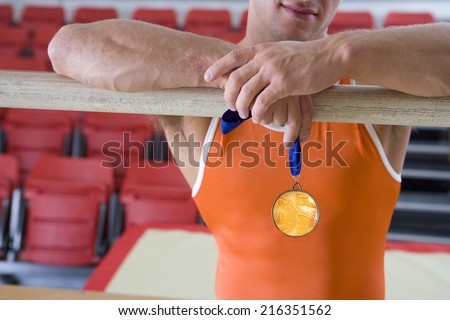 Male gymnast with gold medal, arms on bar, mid section