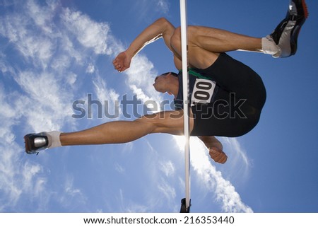 Male athlete jumping over hurdle, view from below