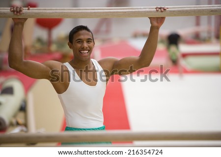 Male gymnast with hands on parallel bars, smiling, portrait