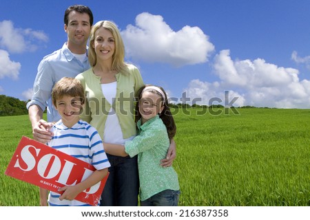Young family standing in field with sold sign