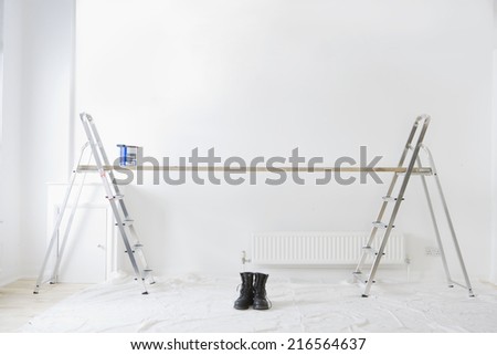 Ladders, wood plank, paint can and work boots in living room
